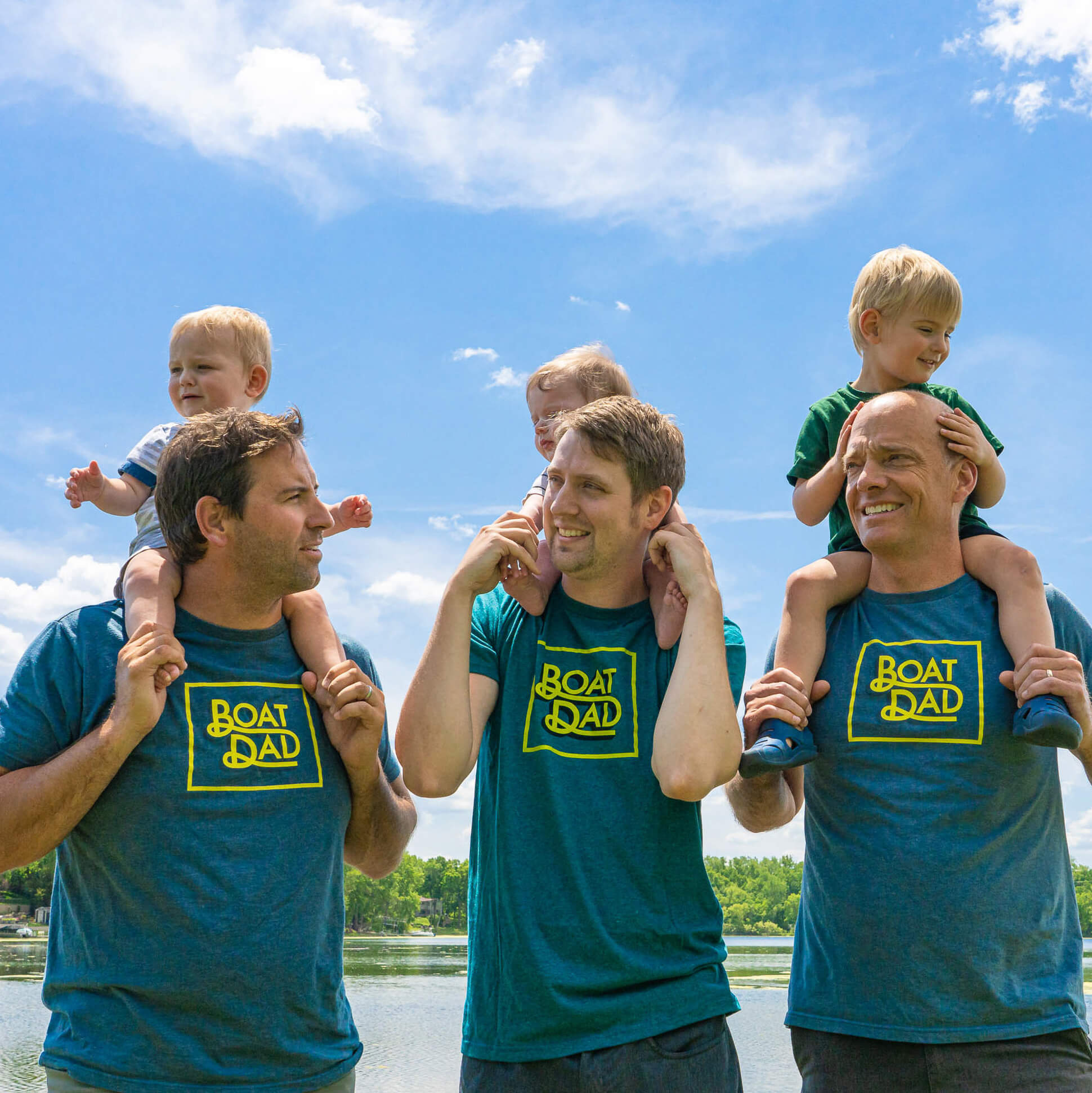 fathers wearing boat dad shirts while holding kids on shoulders